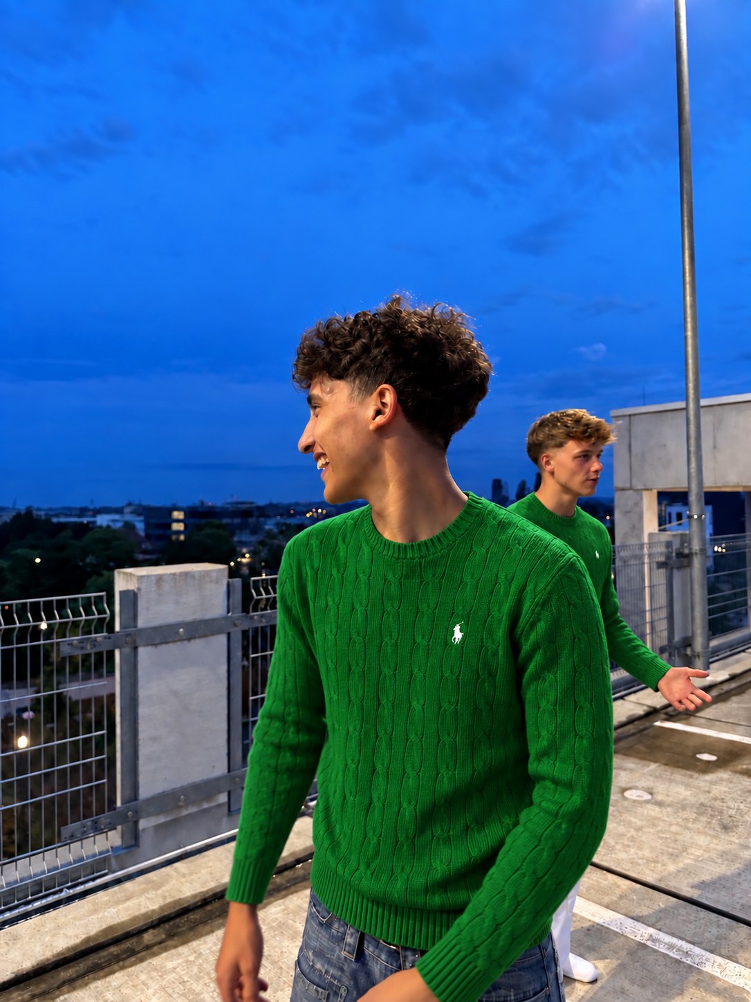 Zwei Freunde in grünen Ralph-Lauren-Pullovern auf einem Dach in der Abenddämmerung